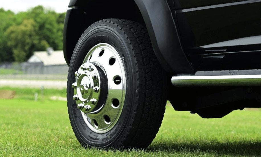 Closeup photo of a front left truck tire on a black truck parked on grass.