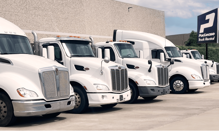 Row of five truck cabs parked outside a building with a PacLease sign in the background.