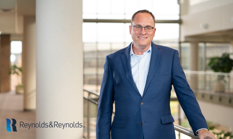 Chris Walsh, president and acting CEO of Reynolds and Reynolds, standing inside an office building wearing a blue suit.