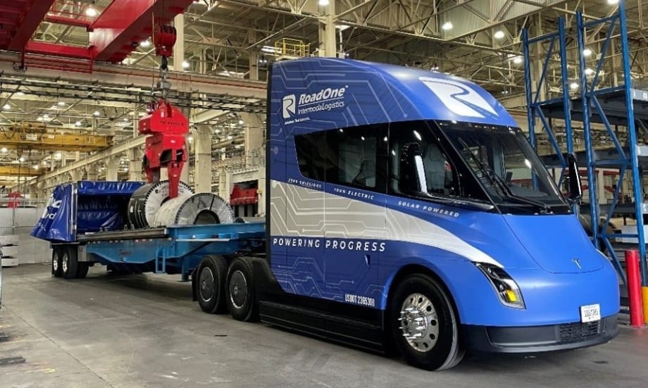 Blue Tesla Semi pulling flatbed trailer inside warehouse or manufacturing facility