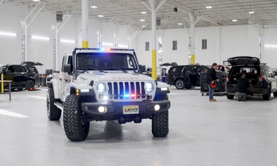 Police Jeep with light activated inside a garage with other vehicles being worked on in the background.