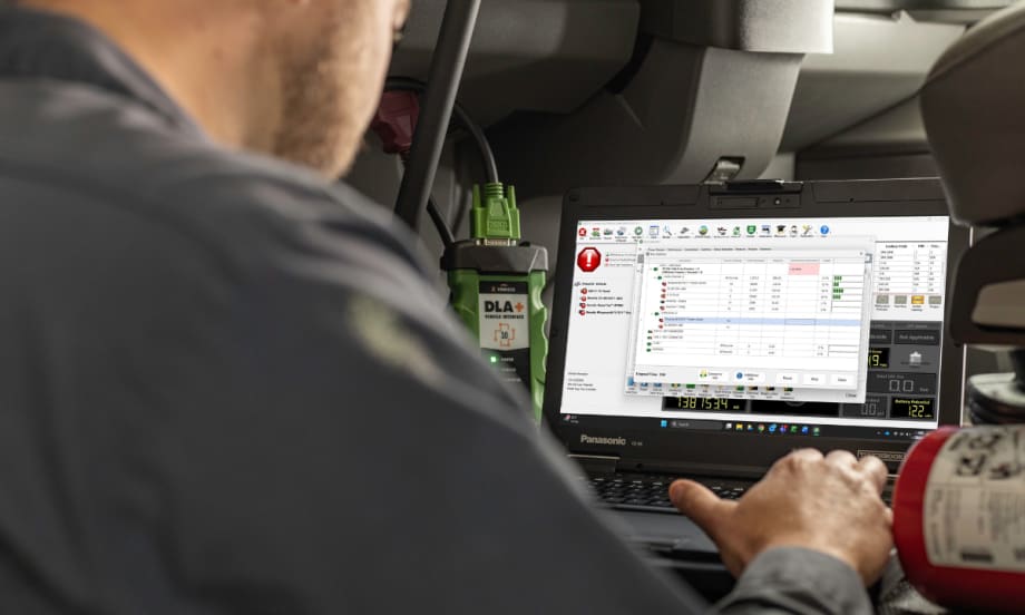 Technician using diagnostic software on a laptop connected to a commercial vehicle to analyze CAN bus data.