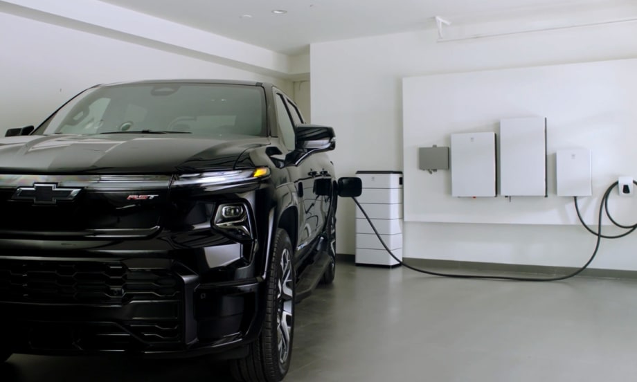 Chevrolet Silverado EV plugged into a home energy system with wall-mounted battery and power management units in a residential garage.