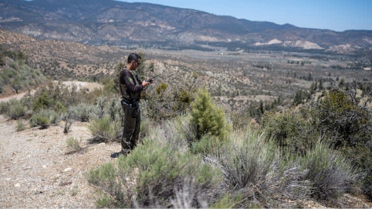 Man standing in desert talking on radio.
