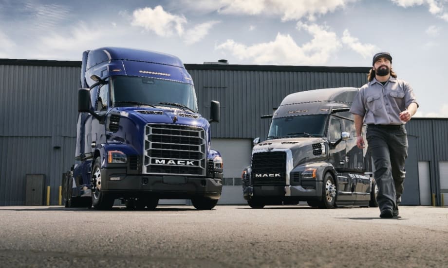 Man walking toward camera with two Mack trucks in the background.