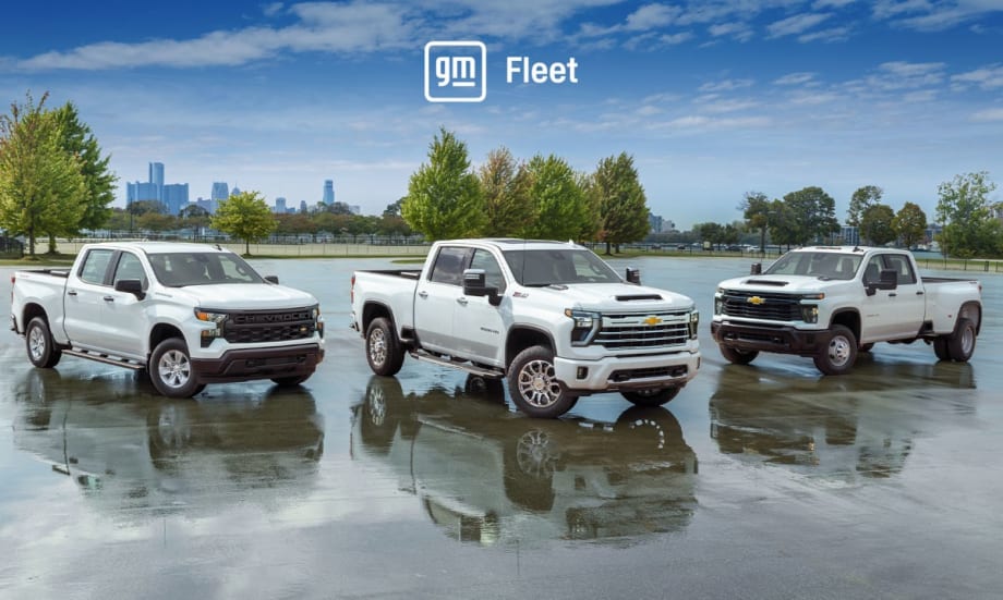 Three white pickup trucks parked in a parking lot with trees in background and a blue sky with logo for GM Fleet.