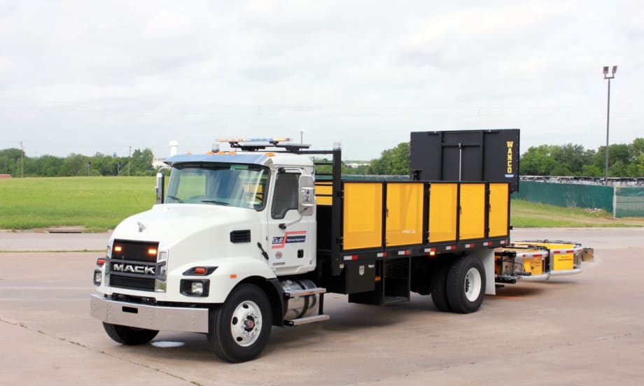 White work truck with yellow bed and yellow rear-mounted crash protection device parked in a parking lot.