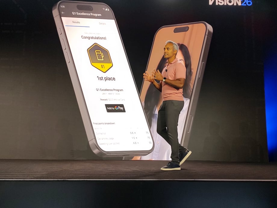 Presenter onstage at Motive Vision 26 conference beside a large smartphone display showing a driver rewards app, highlighting a first-place achievement in a Q1 Excellence Program with points, rankings, and Google Pay integration.