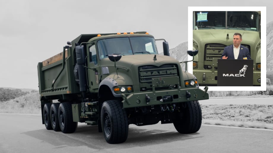 Military-style Mack Defense dump truck parked on a roadway, shown in olive-drab paint with rugged off-road features. An inset photo shows a speaker at a Mack-branded podium in front of the truck during a presentation or announcement.