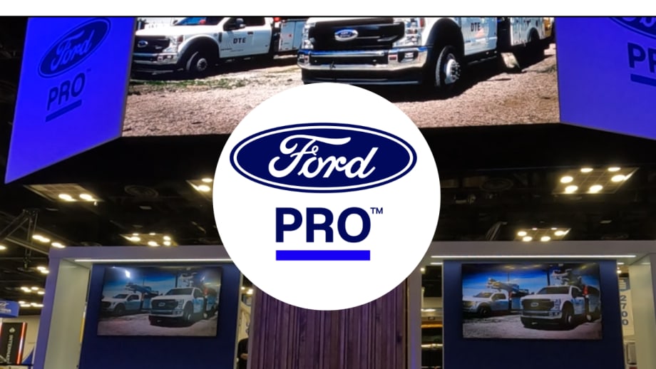 Ford Pro logo over a trade show booth displaying Ford commercial trucks on large digital screens, illustrating the company's commercial vehicle and fleet services showcased at an industry event.