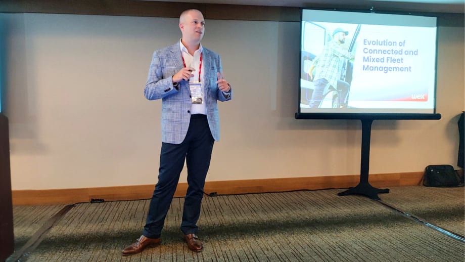 Presenter delivers a WEX conference session on connected and mixed fleet management, speaking beside a presentation screen displaying the topic, “Evolution of Connected and Mixed Fleet Management.”