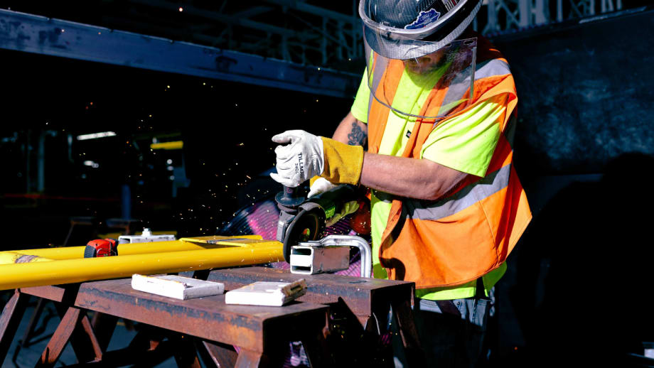 Worker wearing protective gear uses a power grinder on metal equipment inside Ford’s Louisville Assembly Plant.