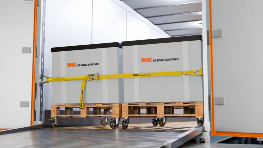 Kinedyne cargo securement strap holds two large containers on wheeled pallets inside a truck trailer, demonstrating a heavy-duty logistics load restraint system.