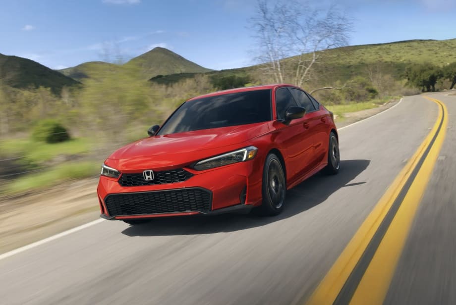 Red Honda Civic hybrid sedan on two lane road with green hills in background