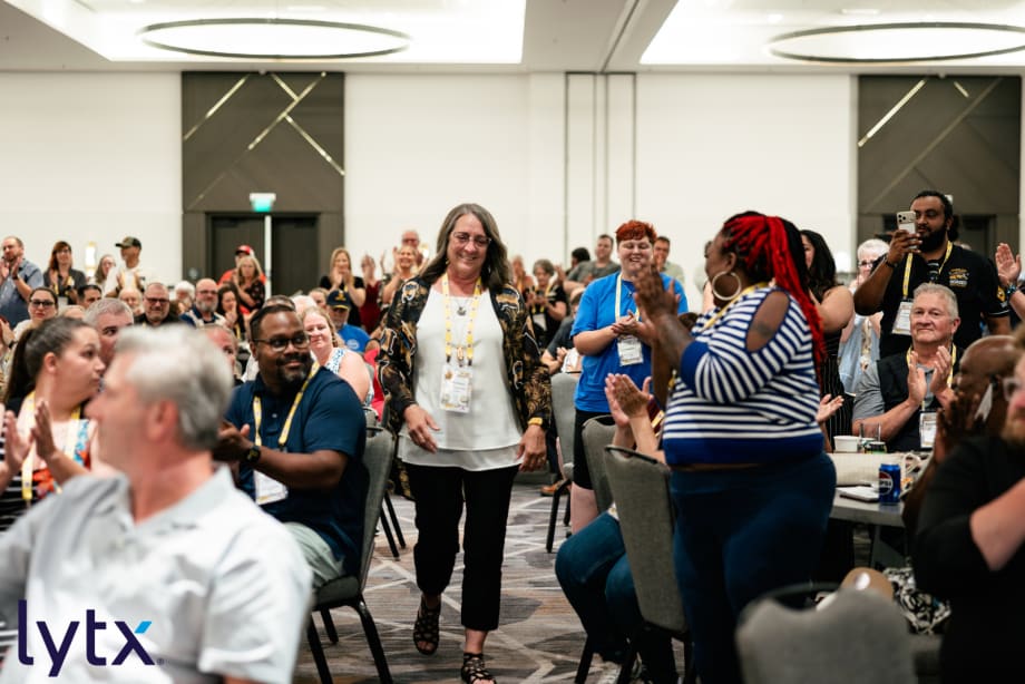 Betty Nelson walks through a standing ovation during an awards ceremony as school transportation professionals applaud her achievements at the event's awards ceremony.