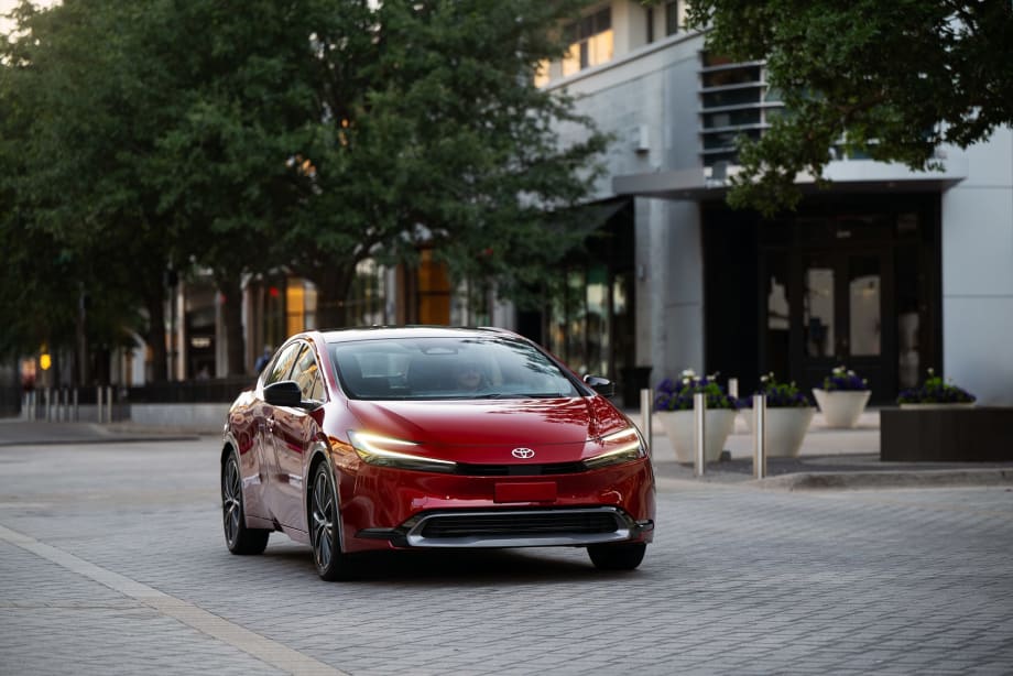 Front three-quarter view of a red 2027 Toyota Prius parked in an urban setting, showcasing the updated hybrid sedan's sleek design, LED lighting and aerodynamic styling.