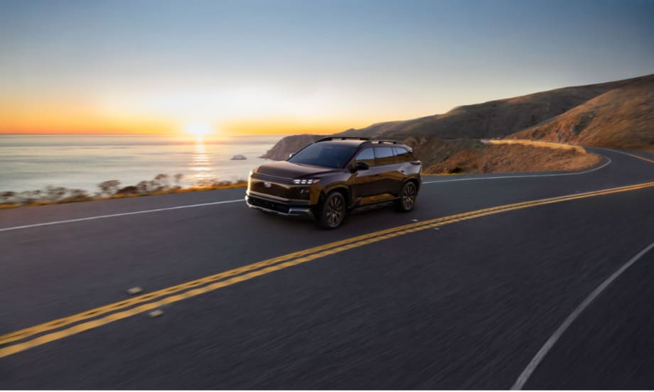 Subaru electric SUV driving along a coastal highway at sunset, representing the 2027 Getaway with three-row seating and all-electric performance.