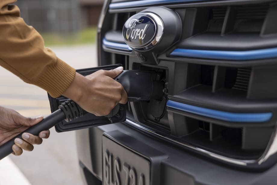 A person is seen plugging in a charger to a Ford F-150 Lightning pickup truck.