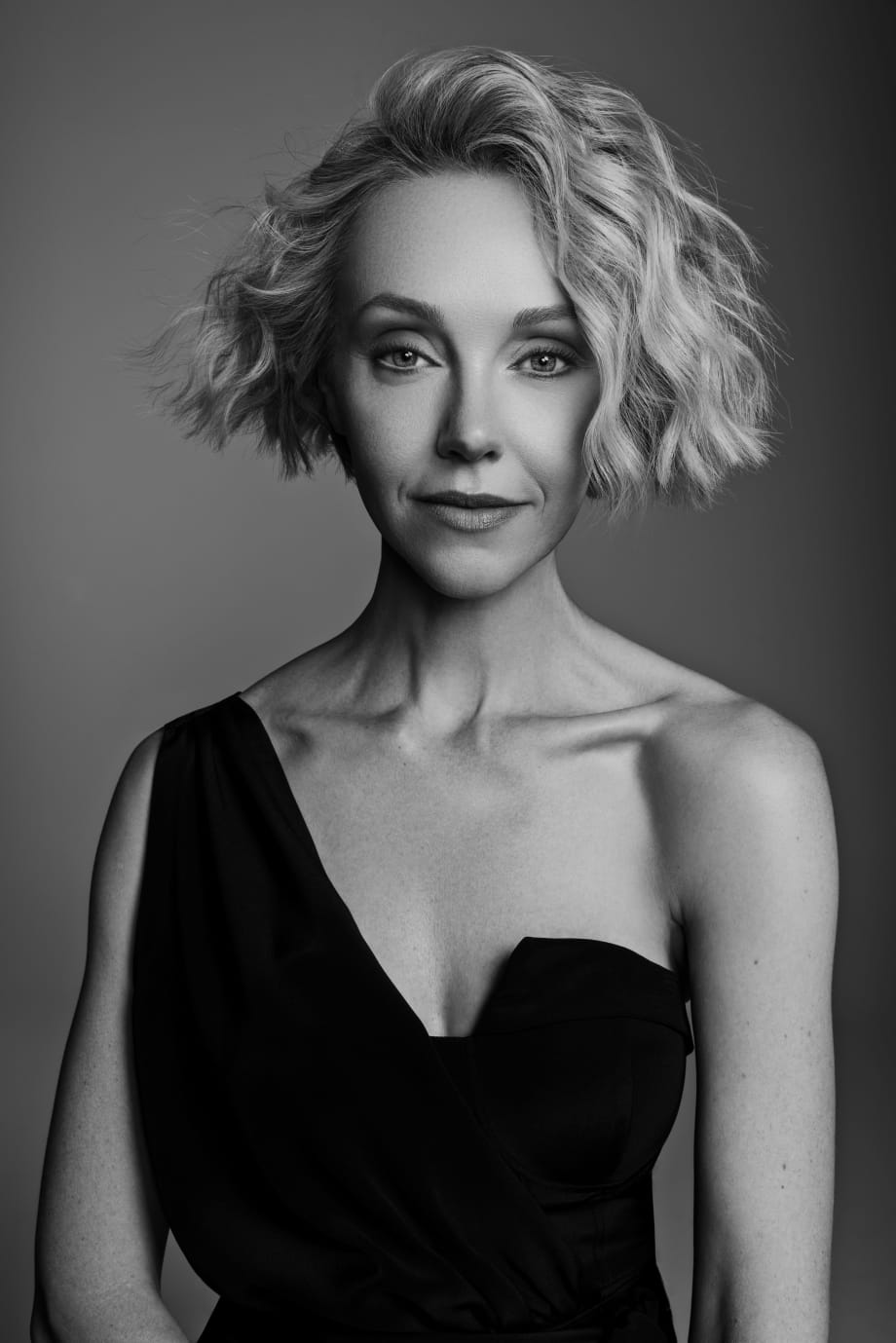 A woman with short blonde hair, wearing a low cut black dress.