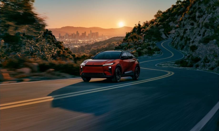 The new 2026 Toyota C-HR BEV driving on a highway with the sunsetting behind it.