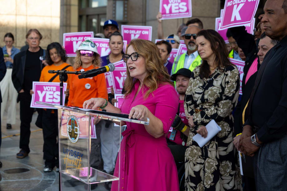 Supervisor and LA Metro Board Member Lindsey P. Horvath stands at a podium with a crowd of community members behind her.