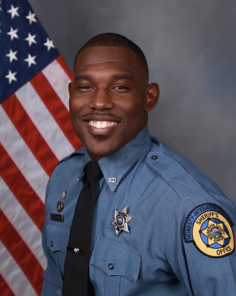 Smiling sheriff's deputy in blue uniform with American flag background