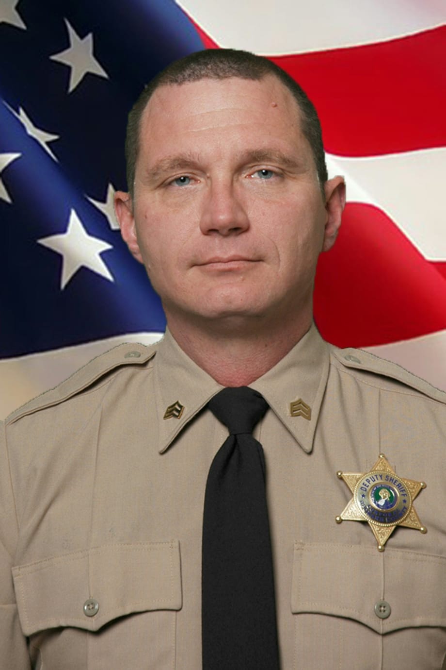 Law enforcement officer in tan uniform with sheriff's badge, standing before American flag
