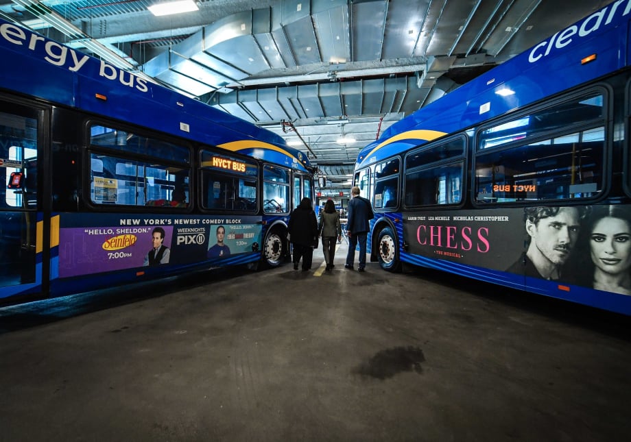 A wide angle view of two MTA buses with three people walking between them.