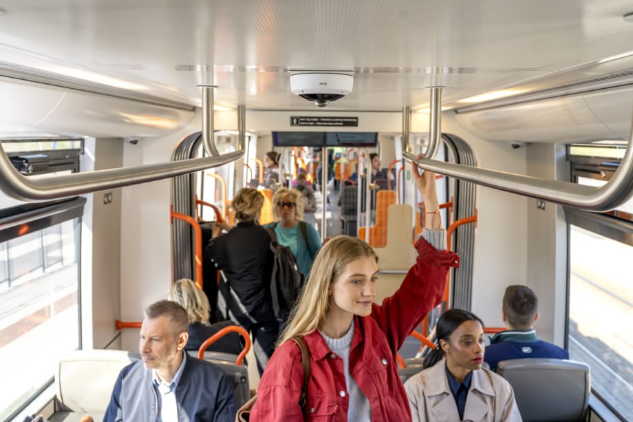 The inside of a rail car with passengers, and a surveillance camera fixed to the ceiling.