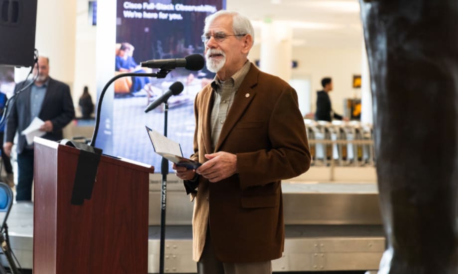 Rod Diridon Sr. speaking at a podium wearing a brown blazer.