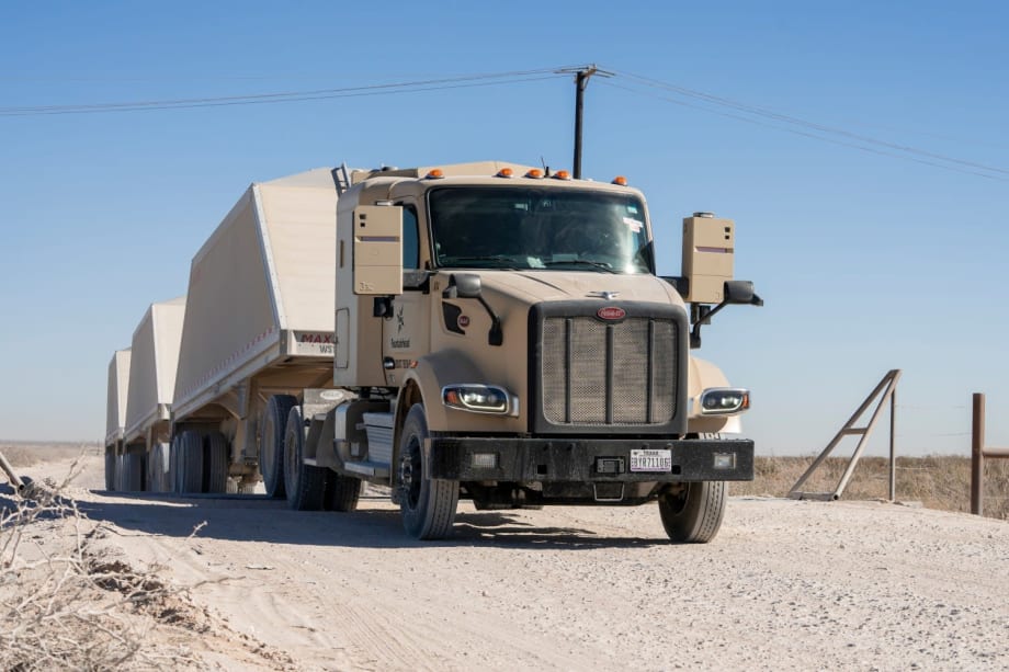 Khaki-colored autonomous Peterbilt truck hauling triple trailers loaded with frac sand for Atlas Energy Solutions in the Permian Basin.