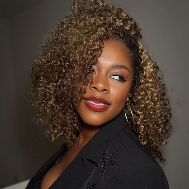 A woman in black, with tight, carmel curls, looks over her shoulder.