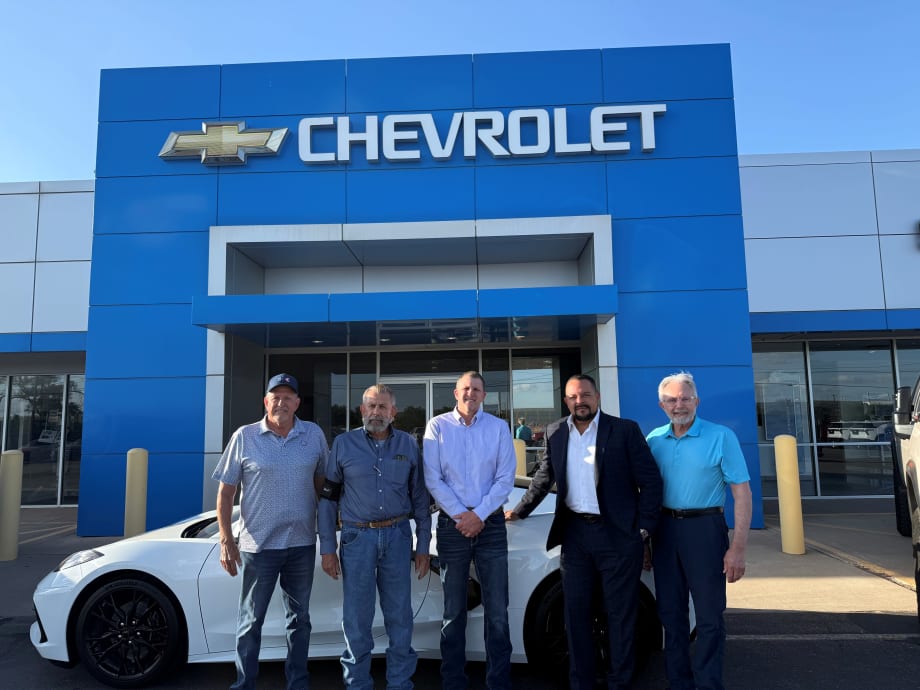 Photo of four men involved in sale of three auto dealerships, standing in front of the sold Chevrolet store