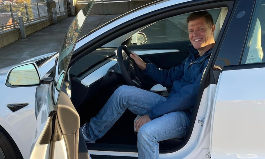 Micah Bergdale sits turned sideways in the driver's seat of a Tesla with the door open.