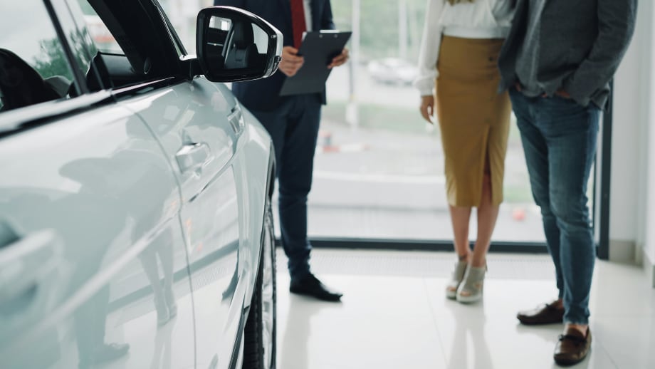 Couple talking with auto salesman next to new car inside dealership