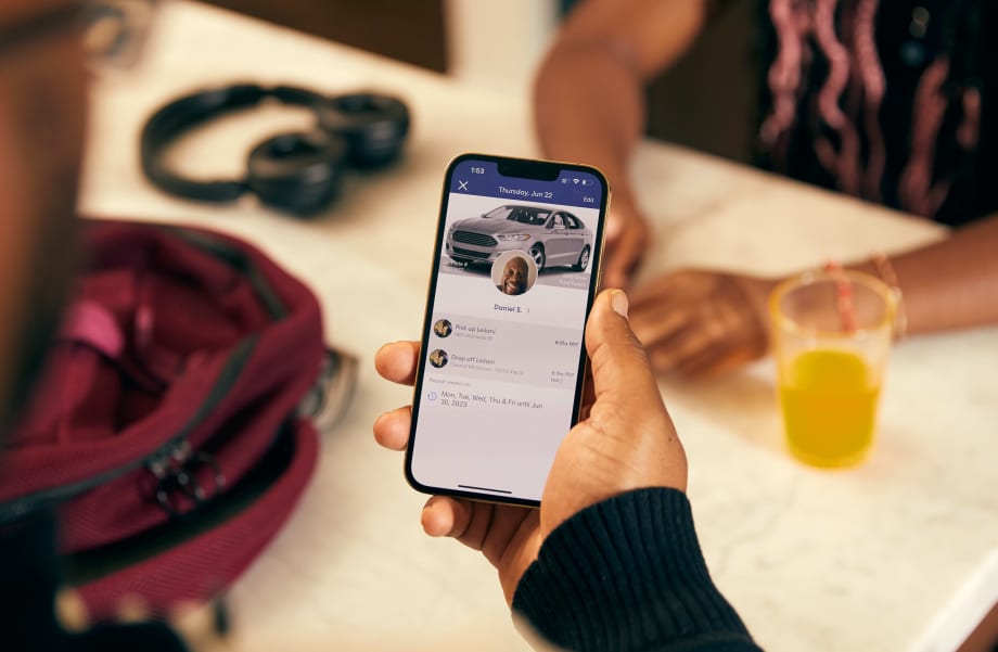 A close up image of a hand holding a phone with HopSkipDrive's platform and CareDriver information on the screen.