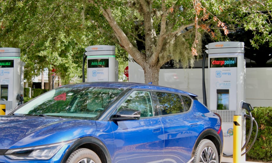 A blue EV backed up against a charging station in a parking lot.