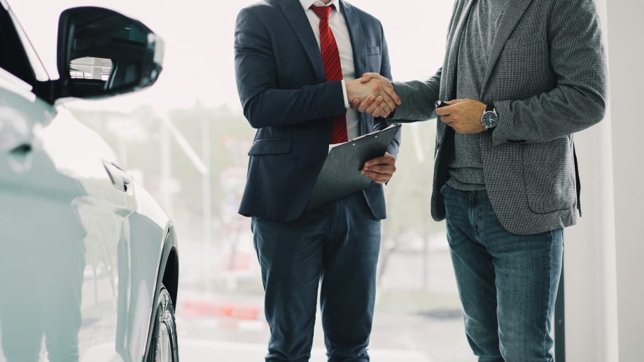 Photo of two businessmen shaking hands next to a white car in a showroom