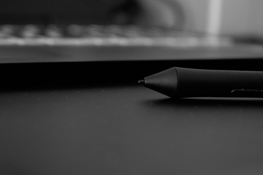 Photo of computer keyboard with a inkpen resting in front of it on the top of a desk