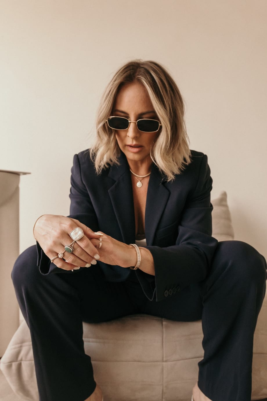 A woman with a short blonde haircut, wearing a suit, sitting, and wearing sunglasses.