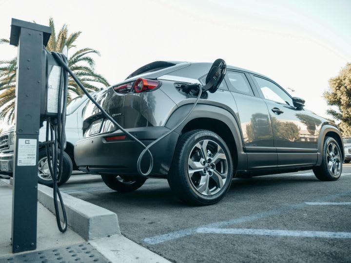 Photo of gray SUV plugged into public electric-vehicle charger in parking lot