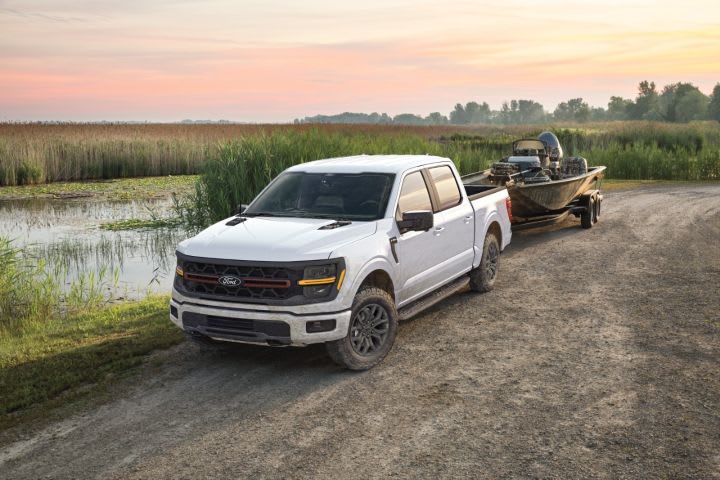 Photo of white Ford F-10 pickup parked on a dirtl road next to a body of water and with a fishing boat hitched to it