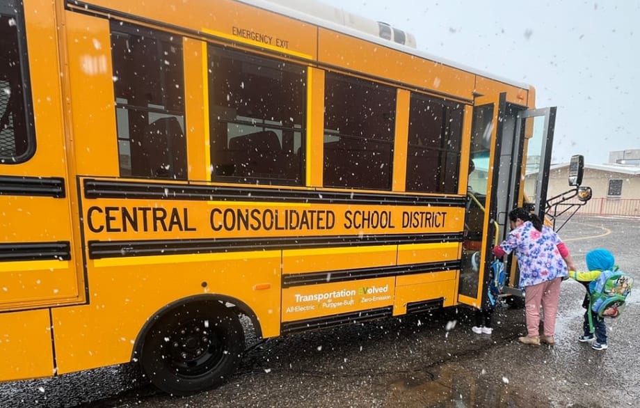 Children board a yellow electric school bus from Central Consolidated School District during snowfall, as an adult assists students at the bus entrance.