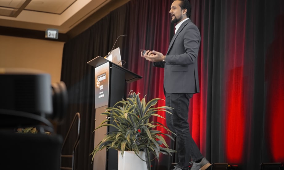 Side view of ICRS speaker Sanchit Garg at podium in front of a floor lit red curtain