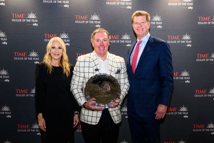 Two men and a woman smiling for photo while center man holds award