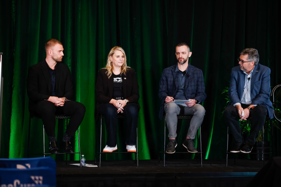 Three men and one woman sitting on a green backlit stage talking