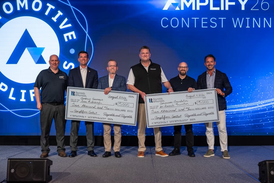 Six men standing on stage receiving two giant $5,000 checks.
