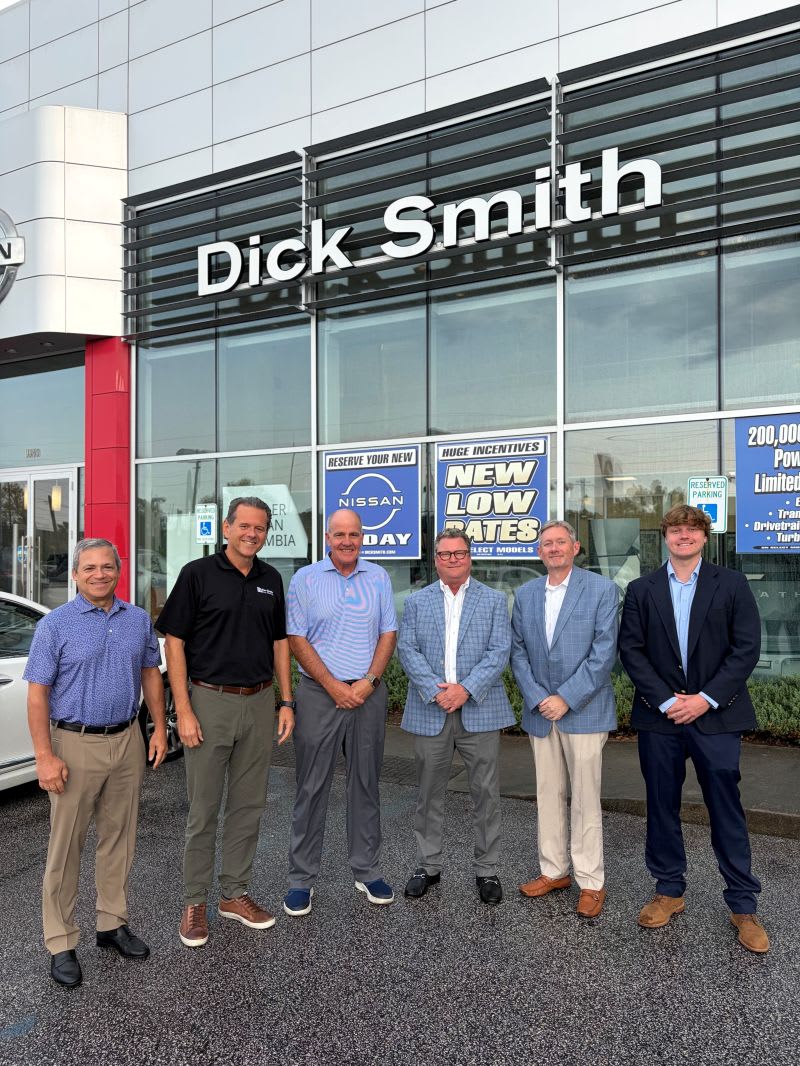 Six men standing for photo outside of car dealership