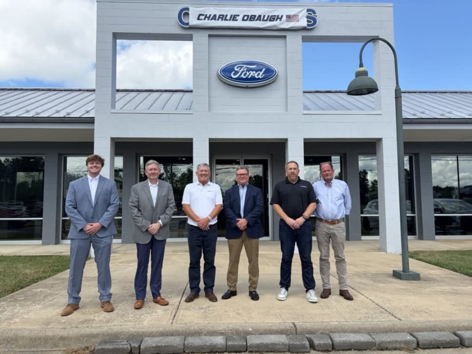 Six men standing in front of a Ford dealership.