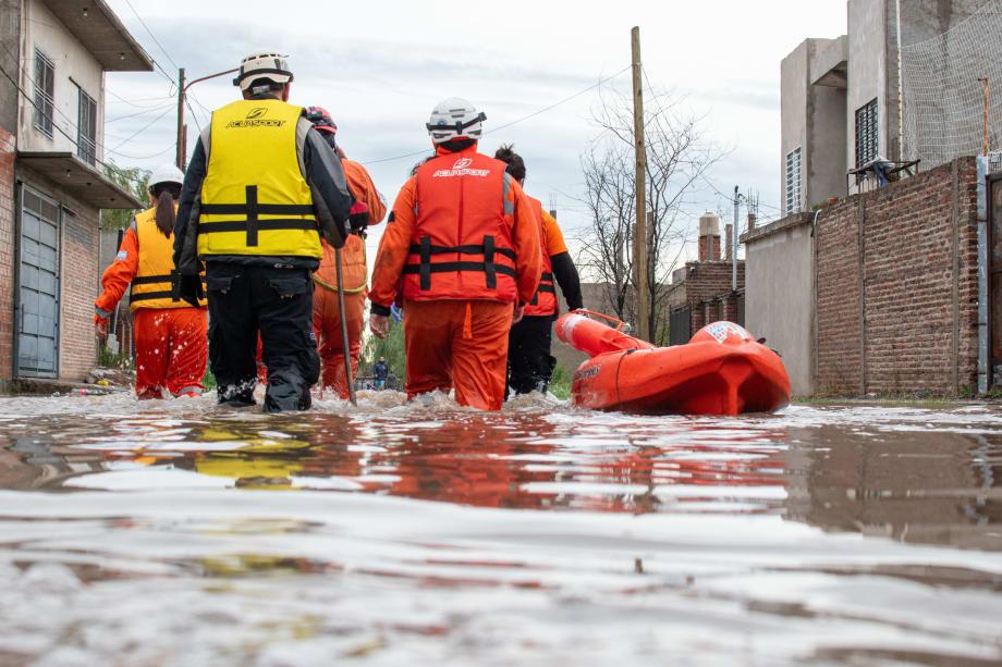 Disaster response team wading through knee deep water with life raft beside them.